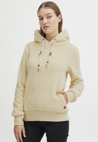 Krämfärgad fleecehuva med en mjuk textur, justerbar dragsko och sidofickor. Ribbad mudd och nederkant. Knappdetalj på sidan.