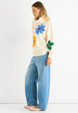 Crème trui met kleurrijke gebreide bloemen; brede blauwe jeans; roze ballerina's; relaxte pasvorm; ribgebreide kraag en zoomdetails.