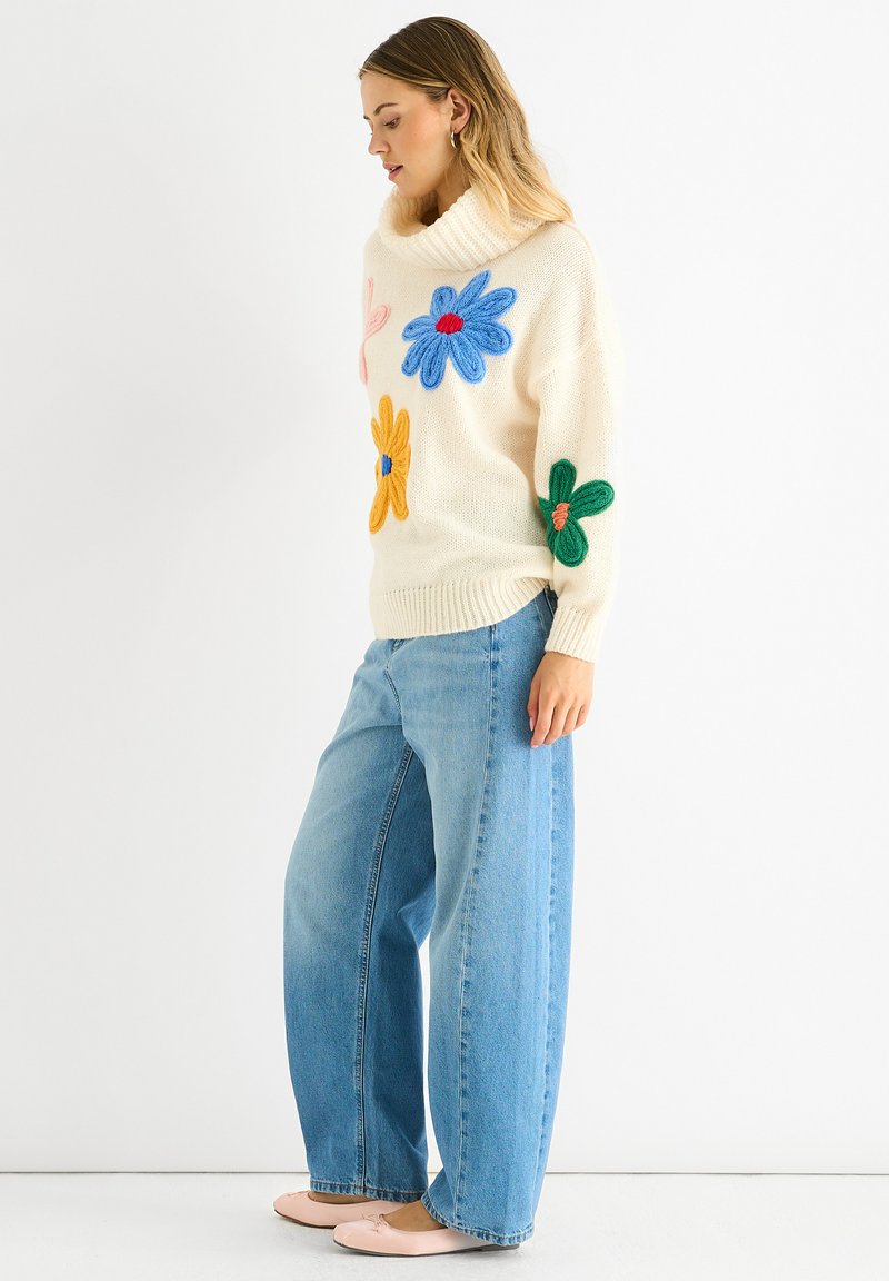 Maglione crema con fiori lavorati a maglia colorati; jeans blu larghi; ballerine rosa; vestibilità rilassata; dettagli con colletto e orlo a coste.