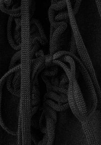 Gros plan sur un tissu en maille noir avec des cordons épais noués en nœud sur des sections froncées et plissées.