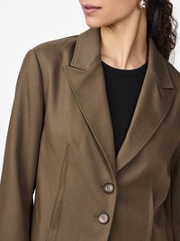 Blazer marron au design structuré, avec deux boutons et un col à cran. Texture lisse, associé à un top noir en dessous.