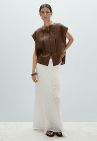 Bruine linnen cropped top met korte mouwen, voorzien van knopen aan de voorkant. Witte textuur maxi rok. Zwarte platform sandalen. Eenvoudige armbanden.