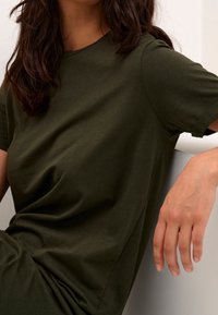 Oliivivärvi lyhythihainen t-paita, pyöreä pääntie, pehmeä kangas, rento istuvuus, jossa on sileä pinta ja hienovaraiset saumat sivuilla.