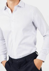 Gestreepte langarmlige shirt in lichtblauw en wit, met knopen aan de voorkant, een klassieke kraag en een zachte textuur. Gecombineerd met donkere broeken.