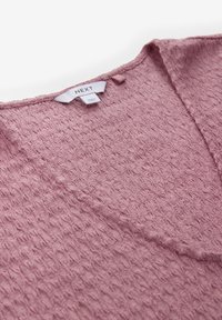 Top a maniche corte, rosa chiaro, con motivo testurizzato e scollo a V, con etichetta di marca sulla parte posteriore. Realizzato in tessuto morbido.