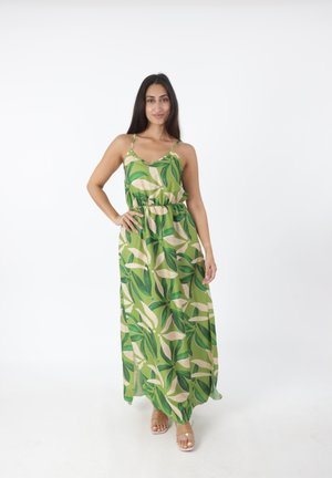 Robe maxi en tissu vert avec des motifs de feuilles ; dotée de fines bretelles, d'un décolleté en V et d'une taille élastique pour un ajustement ample. Sandales visibles.