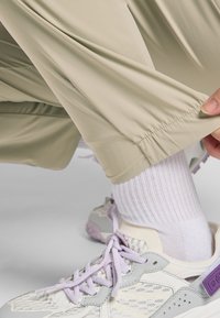 Beige, lichte broek met een elastische manchet, gecombineerd met witte ribbelkousen en grijze schoenen met paarse accenten en een gestructureerd ontwerp.