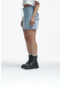 Woman wearing a light blue denim skirt and black lace-up platform boots with white socks on a white background.