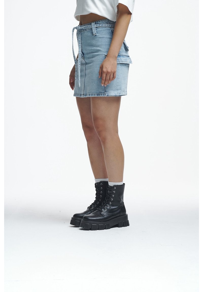 Woman wearing a light blue denim skirt and black lace-up platform boots with white socks on a white background.