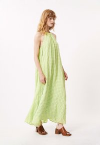 Maxi-Kleid in Hellgrün, aus strukturiertem Stoff mit Karomuster. Halterneck-Design, fließende Silhouette, kombiniert mit braunen Sandalen mit Absatz.