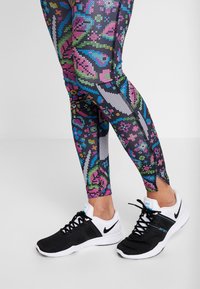 Leggings negras con un patrón de diseños geométricos multicolores, combinados con zapatillas deportivas en blanco y negro con un acento azul.
