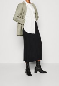 Zelený kostkovaný blejzer, bílá košile na knoflíky, černá plisovaná midi sukně a černé kotníkové boty se čtveratou špičkou a blokovým podpatkem.