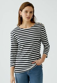 Schwarz-weiß gestreifter Langarm-Top mit weitem Ausschnitt und Knopfakzenten an der Schulter, kombiniert mit blauen Jeans. Weiche Stofftextur.