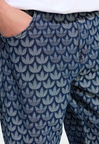 Džínsy s tmavomodrým základom a opakujúcim sa vzorom listov v svetlomodrej farbe. Obsahujú bočné vrecká a tonálne švy.