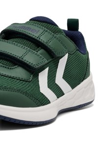 Grüner Sportschuh aus Netz- und Leder-Materialien, mit Klettverschlussriemen und weißen Streifen. Nahaufnahme des Zehenbereichs des Schuhs.