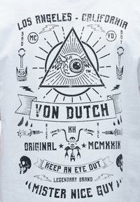 Μαύρο γραφικό σχέδιο σε λευκό πουκάμισο με πανόπτη οφθαλμό μέσα σε τρίγωνο, κρανία, μέρη μοτοσυκλέτας και κείμενο που περιλαμβάνει "Von Dutch" και "Los Angeles California."