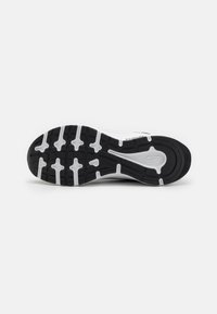Suela de zapatilla en blanco y negro con surcos profundos, que presenta un patrón texturizado, refuerzo en el talón y un diseño flexible para mayor tracción.