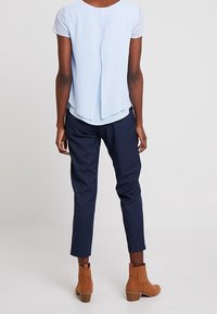 Light blue, short-sleeve top with a high-low design; navy pinstriped, tapered pants, and brown ankle boots with a textured finish.