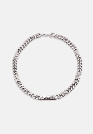 Zilveren ketting met dikke schakels en een rechthoekig label met de gravure "Ed Hardy" op een witte achtergrond.