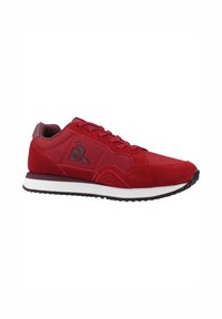 Zapatilla deportiva roja que combina materiales de ante y sintéticos, con puntera redonda, diseño con cordones y una suela blanca en contraste.