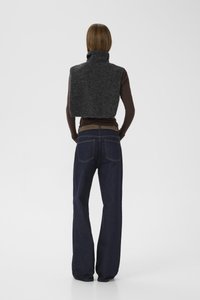 Gilet en polaire gris foncé, design à col montant, longueur cropped, porté par-dessus une chemise à manches longues marron. Assorti avec un jean en denim foncé à coupe ample.