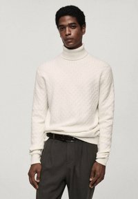 Pulover alb din tricot cu guler înalt, având un model texturat în formă de diamant, asortat cu pantaloni închiși la culoare și o curea neagră. Design curat și modern.