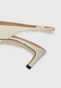 Talons slingback en cuir beige au grain lisse, au design minimaliste, à la forme effilée et avec un accent de talon noir contrastant.