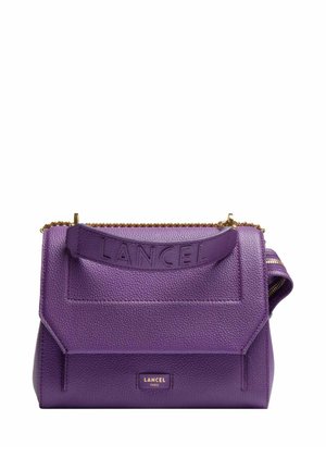 Sac à main Lancel en cuir grainé violet avec une lanière embossée du logo, un détail en chaîne dorée et une étiquette Lancel Paris sur le rabat avant.