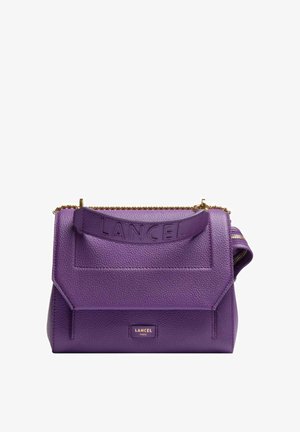Sac à main Lancel en cuir grainé violet avec une lanière embossée du logo, un détail en chaîne dorée et une étiquette Lancel Paris sur le rabat avant.