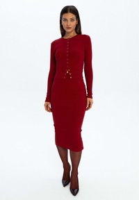 Czerwony prążkowany zestaw dwóch części, składający się z bluzki z długim rękawem zapinanej na guziki oraz dopasowanej spódnicy midi, w połączeniu z czarnymi szpilkami.