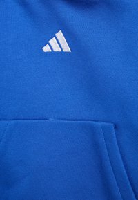 Haut à capuche bleu avec une poche avant et un logo Adidas blanc dans le coin supérieur gauche, fabriqué à partir d'un tissu lisse et texturé.