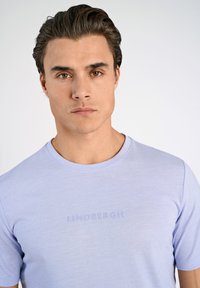 Ljuslila t-shirt med korta ärmar, rund halsringning och präglad "LINDBERGH"-logotyp på bröstet. Slät tygtextur.