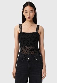 Schwarzer Spitzen-Body mit floraler Stickerei, durchsichtigen Einsätzen und breiten, dekorativen Trägern; kombiniert mit hoch taillierten schwarzen Jeans.