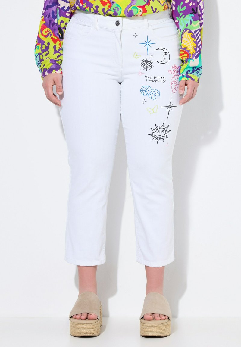 Valkoiset farkut, joissa on mustia, sinisiä ja pastellivärisiä brodeerattuja kuvioita, joissa on taivaallisia ja leikkisiä teemoja edessä.