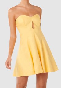 Šaty bez ramínek žluté barvy se srdcovým výřezem a otvorem ve tvaru klíče, přiléhavé v oblasti těla s rozšířenou sukní.