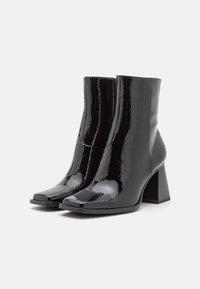 Botines de charol negro con punta cuadrada, tacón bloque y textura suave; diseño elegante con una silueta minimalista.