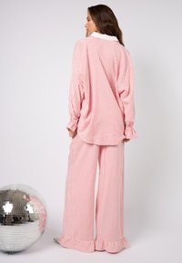 Zestaw do relaksu w czerwono-białe paski, składający się z koszuli z kołnierzykiem w oversize i szerokich spodni. Miękka tkanina z marszczonymi mankietami i rozkloszowanym dołem.