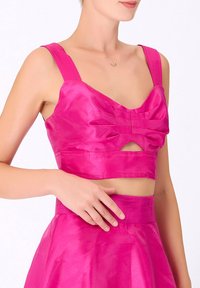 Top court en satin fuchsia avec bretelles larges, détail de nœud au centre et une découpe sous la poitrine, assorti d'une jupe correspondante.