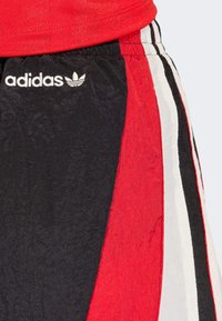 Crne, crvene i bijele sportske hlače od teksturiranog tkanog materijala. Imaju elastični pojas i adidas logo na lijevoj strani.