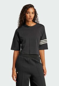 Čierna skrátená tričko s krátkymi rukávmi, s tromi bielymi pruhmi na ľavom ramene. Vyrobené z mäkkej tkaniny, navrhnuté pre pohodlie.