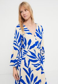 Rochie tip petrecută cu model de frunze albastre, dintr-un material ușor, cu decolteu în V, mâneci lungi clopot și detaliu cu talie legată.