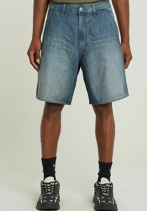 Hellblaue Denim-Shorts mit einem ausgewaschenen Finish, mittelhoher Taille und fünf Taschen, kombiniert mit schwarzen Sportschuhen und Kniestrümpfen.