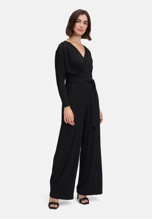 Tutina nera con maniche lunghe, scollatura a V profonda e cintura legata in vita. Design a gamba larga, realizzata in un tessuto liscio, presenta dettagli minimi.