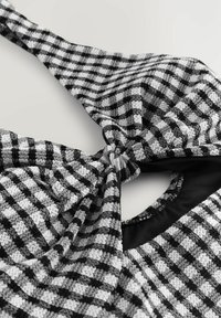 Svart- och vitrutigt tygtop med en knuten design, texturerad yta och en kontrasterande svart foder vid halsringningen.