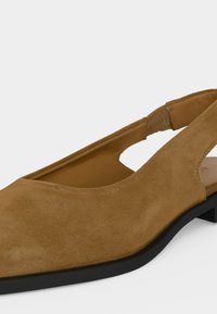 Καφέ καστόρινο παπούτσι με μυτερή μύτη, λουράκι στο πίσω μέρος και μαύρη σόλα σε λευκό φόντο.