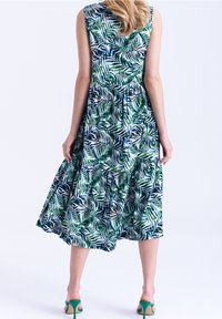 Vestido de estampado floral con patrones de hojas de palma verdes y azules, diseño sin mangas, cintura fruncida y falda en capas, combinado con tacones verdes.