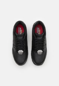 Zapatillas negras de cuero con un acabado texturizado, que cuentan con un diseño de cordones y etiquetas de marca prominentes para mayor resistencia al deslizamiento y espuma viscoelástica.