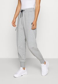 Graue Sweatpants mit elastischen Bündchen, einem Bund mit Kordelzug und schwarzem Logodetail am Oberschenkel, kombiniert mit weißen Sneakern.