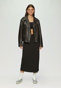 Zwarte leren motorjack met zilveren ritsen, zwart crop top en lange zwarte rok met een zijsplit. Zilveren sneakers en witte enkelsokken.