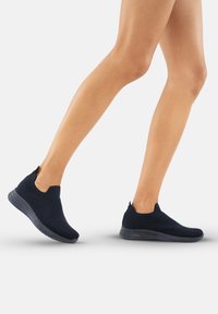 Le scarpe slip-on nere in maglia presentano un design testurizzato, aperture elastiche e una suola traslucida flessibile, ideali per comfort e facilità d'uso.